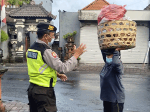 Ipda I Ketut Sukarata membantu seorang ibu mengangkat keranjang barangnya, wilayah hukum Polres Badung,Minggu (22/1) pagi.